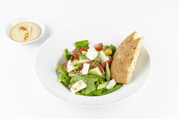 Greek salad with feta cheese, Ligurian olives and tortilla pea and hummus on a plate on a white background