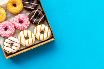 Glazed decorated donuts in box on blue background flat lay mock up