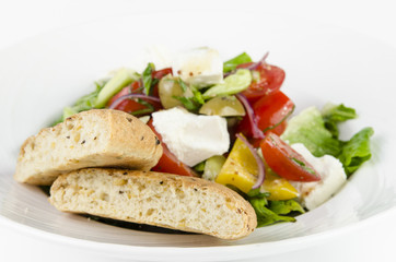 Greek salad with feta cheese, Ligurian olives and tortilla pea and hummus on a plate on a white background