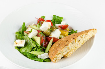 Greek salad with feta cheese, Ligurian olives and tortilla pea and hummus on a plate on a white background