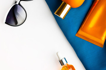 Orange mock up bottles of sun screen and sunglasses on bright contrast blue beach wrap on horizontal empty white background with copy space. Holiday flat lay