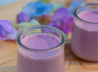 Homemade milk sweet yogurt with bilberry. Blueberry yogurt in glass jars on wooden table in summertime. Dessert. Color lavender. Evening light. Soft focus. Blurry background. Macro. Top view