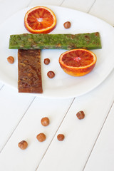 Eastern sweet churchkhela, a half of red orange and hazelnuts on a white surface of painted boards. Daylight. Shallow depth of field