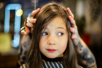 a cute girl sits in a hair salon her head held still by a hairdresser