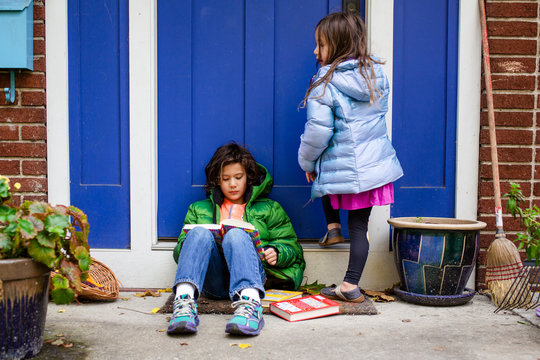 A young boy sits on his front stoop with his sister reading