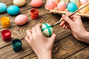 Fototapeta na wymiar partial view of girl decorating easter eggs with paintbrush at wooden table