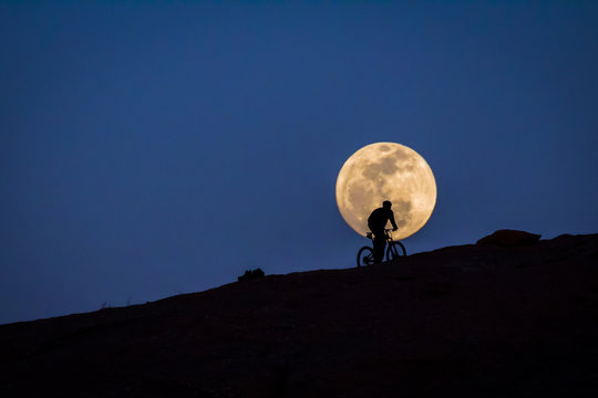 Silhouetted bike rider riding in front of a full moon.