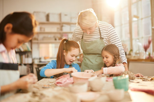 Portrait of female art teacher working with children in pottery class, scene lit by serene sunlight, copy space