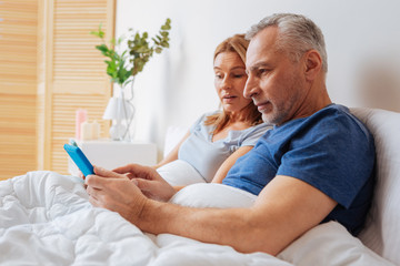 Grey-haired husband showing morning news on tablet to his wife