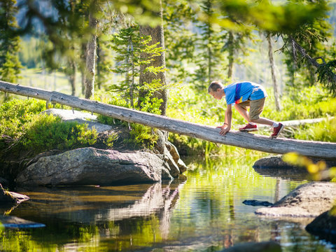 Young boy climbing log over stream, McCall, Idaho, USA