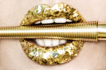 Gold passion lips with white teeth close-up. Macro of lips with creative make-up with gold lipstick and brush