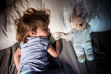 Young girl sleeping with teddy bear in bed