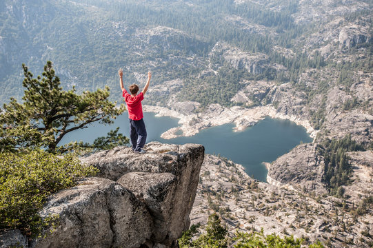 A boy  wearing red t shirt looks from above the Donnell Lake sorrounded by trees and rocks , along the Sonora Road.