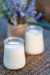 Milk yogurt in glass jars on wooden table in summertime. Homemade milk sweet yogurt. Dessert. Lavender flowers. Summer twilight. Soft focus. Blurry background. Close-up. Copy space.
