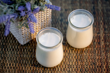 Milk yogurt in glass jars on rustic table in summertime. Homemade milk sweet yogurt. Dessert. Lavender flowers. Evening light. Soft focus. Blurry background. Close-up. Top view. Copy space.