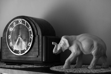 Porcelain elephant figure standing next to old, retro clock. Concept of memory and time passing by. 
