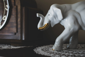 Porcelain elephant figure standing next to old, retro clock. Concept of memory and time passing by. 