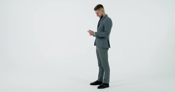 Full length portrait of Caucasian business man in suit texting on his phone against white background. 4K UHD