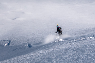 Single woman skier descending a remote alpine untracked powder slope