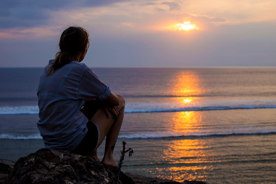 Woman sitting on rock at the beach and looking sunset view