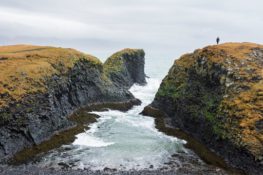 Hiker walking on grassy cliff, Arnastapi, Iceland