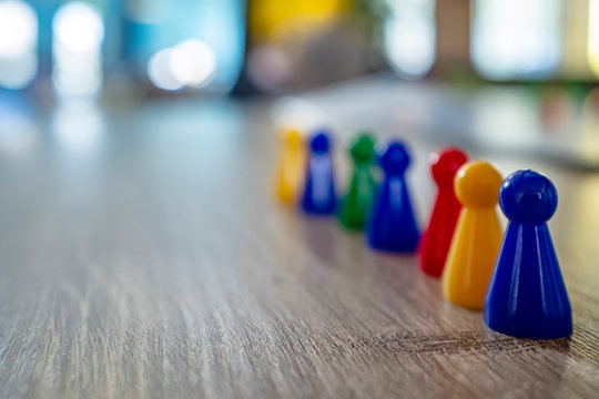 Child put in one row multicolored plastic chips from a board game on a wooden table, in natural light, on a blurred background.