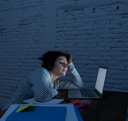 Close up portrait of a overworked and tired young woman studying late at night on moody light.