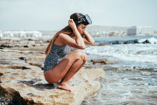 woman in a swimsuit and diving googles playing with the waves on the beach