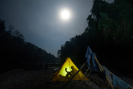 Man camping in tent at night on the Nam Ou River in Phou Den Din National Protected Area, Phongsaly, Laos