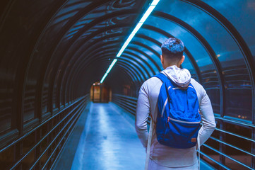 Young student man walking and looking through moody blue dark tunnel