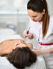 Closeup. Cosmetician is preparing patient for a cosmetic procedure. She gently applies a composition with a brush