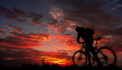 Fototapeta na wymiar cyclist with a bicycle, in the background fiery sunset.