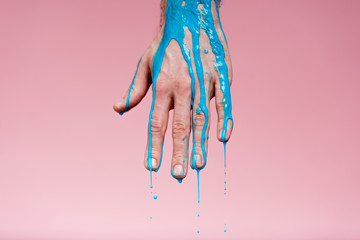 cropped with of male hand with spills of blue paint on pink