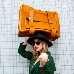 woman in hat and green cloak in 90s style with travel suitcase and piggy bank