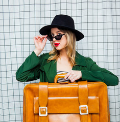 woman in hat and green cloak in 90s style with travel suitcase
