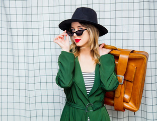woman in hat and green cloak in 90s style with travel suitcase