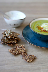 Creamy vegetable soup with kale, cabbage, celery and millet, decorated with olive oil, yoghurt sauce and chilli flakes. Served with seed crackers and lemony yoghurt sauce. Selective focus.