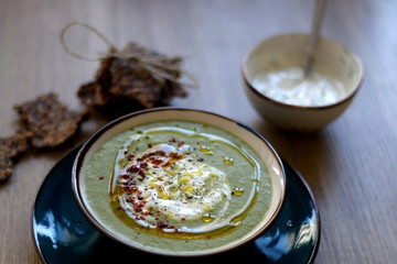 Creamy vegetable soup with kale, cabbage, celery and millet, decorated with olive oil, yoghurt sauce and chilli flakes. Served with seed crackers and lemony yoghurt sauce. Selective focus.