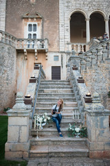 Fototapeta na wymiar Bari, Puglia, Italy, 07 November 2018: Young romantic tourist girl sitting on the old stone stairs in the castle garden