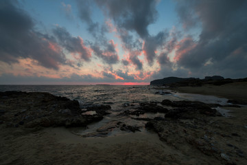 Pink and blue sunset on the beach in Creta, Greece. Beach with blacks rocks and waves at dusk