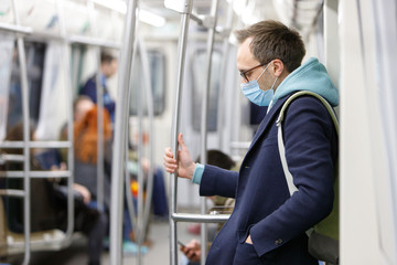 Fototapeta na wymiar Exhausted man in eyeglasses feeling sick, wearing protective mask against transmissible infectious diseases and as protection against the flu in public transport/subway, people on background. 