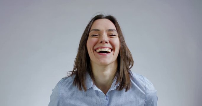Beautiful Caucasian female laughing and looking into camera against grey background. 4K UHD