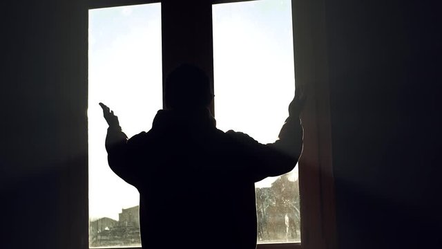 Silhouette man stand lifts his hands up near window in dark room sunshine jalousie installing apartment interior inside sunlight view closeup flat slow motion