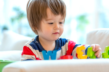 Happy little toddler boy playing with alphabet letters blocks