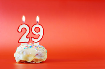 Twenty nine years birthday. Cupcake with white burning candle in the form of number 29. Vivid red background with copy space