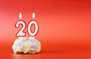 Twenty years birthday. Cupcake with white burning candle in the form of number 20. Vivid red...