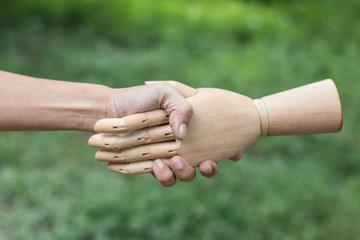 Wooden hand and men hand in handshake to show friendship and respect on nature background
