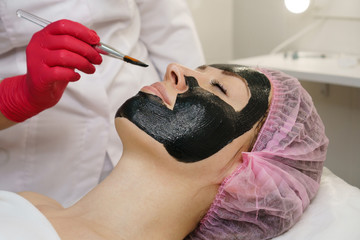 Obraz na płótnie Canvas Beautician apply black moisturizing mask on girl's face. Anti-aging procedure