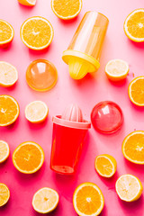 Orange and lemon juice maker, fresh summer juice, cut lemon and orange fruit with red and yellow juice container and squeezer,top view, on a pink board with strong backlight