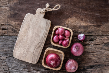 Top view of herbal vegetable ingredients, fresh red onion and empty chopping board on old wooden table, cooking preparation concept